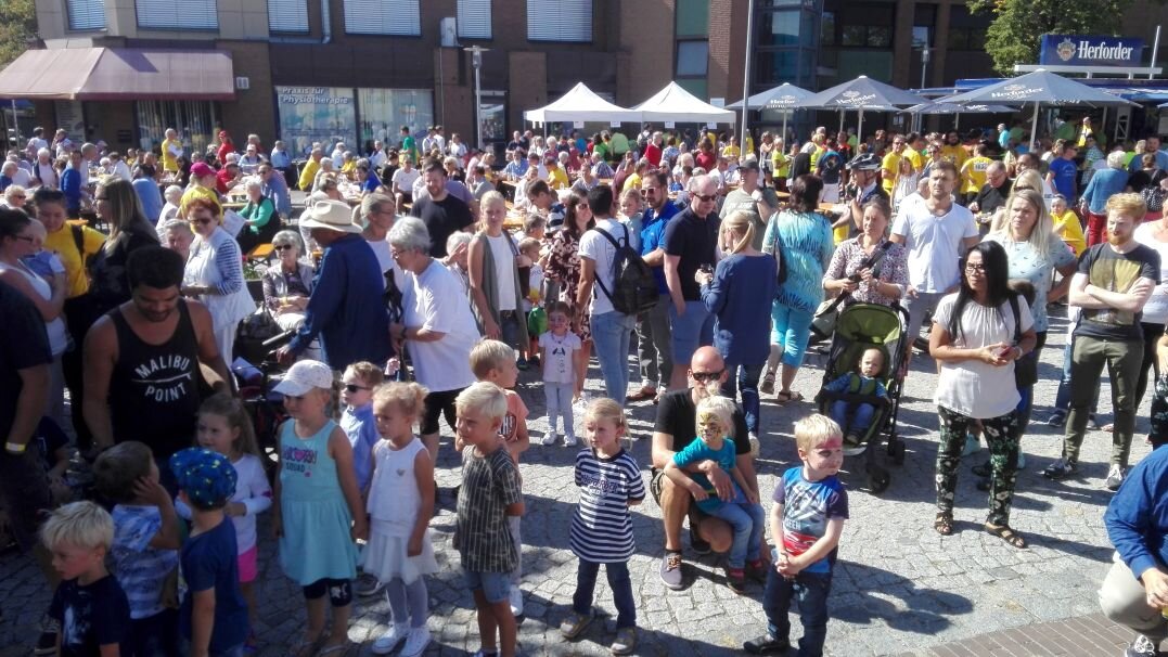 Auf diesem Foto sehen Sie einen Platz, auf dem sich viele Menschen unterschiedlichen Alters befinden