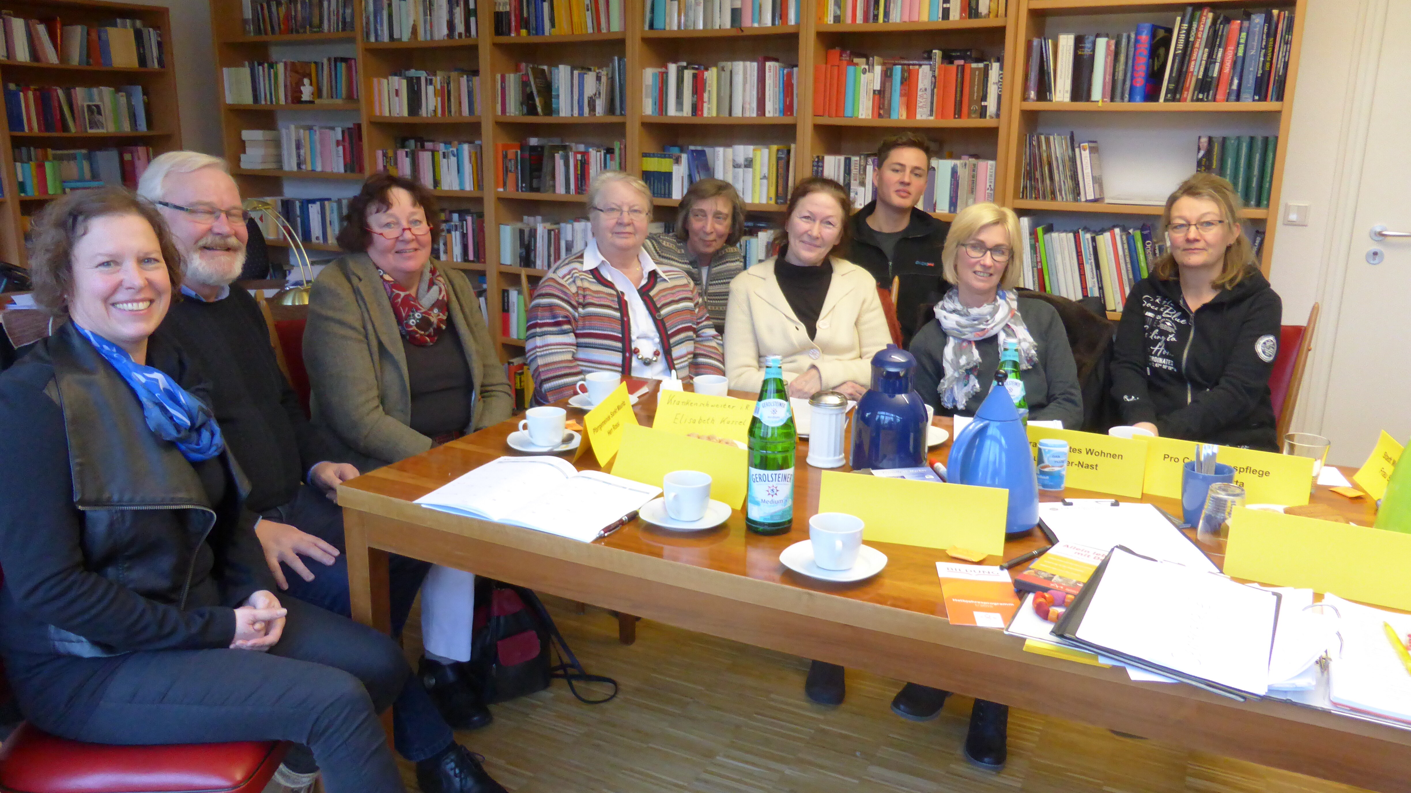 Mehrere Personen, die an einem Tisch sitzen. Im Hintergrund stehen viele Bücherregale.