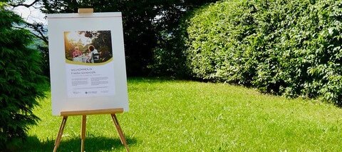 Im Garten steht eine Flipchart. Darauf ist ein Begrüßungsplakat für Friedas Gartencafé 