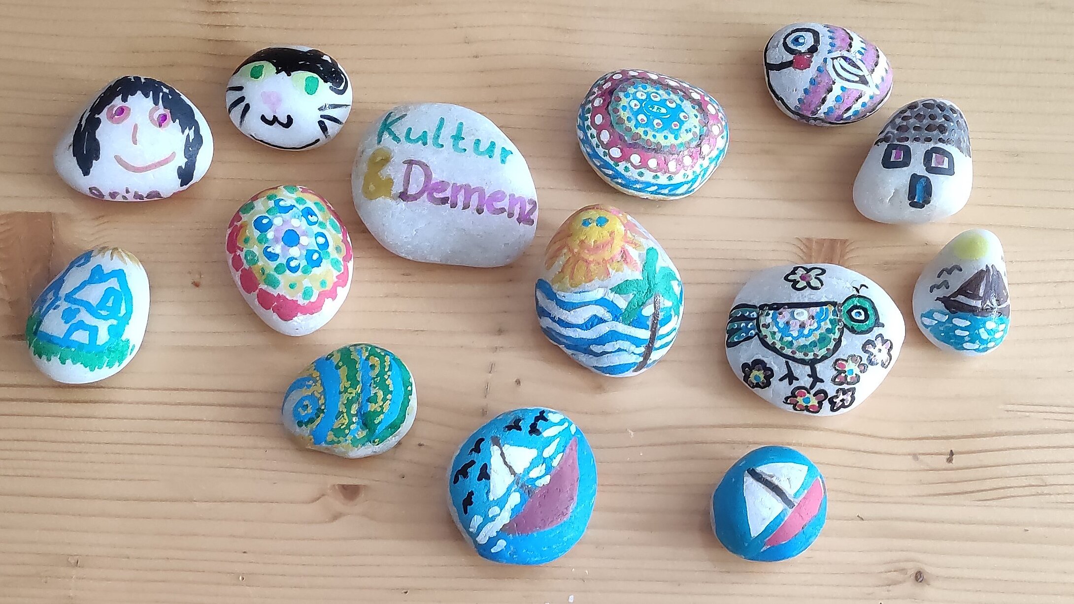 © Kathrin Schulz-Jokiel Vogelperspektive: Mehrere bunt bemalte Steine liegen auf einem Tisch. Auf einem Stein steht "Kultur & Demenz".