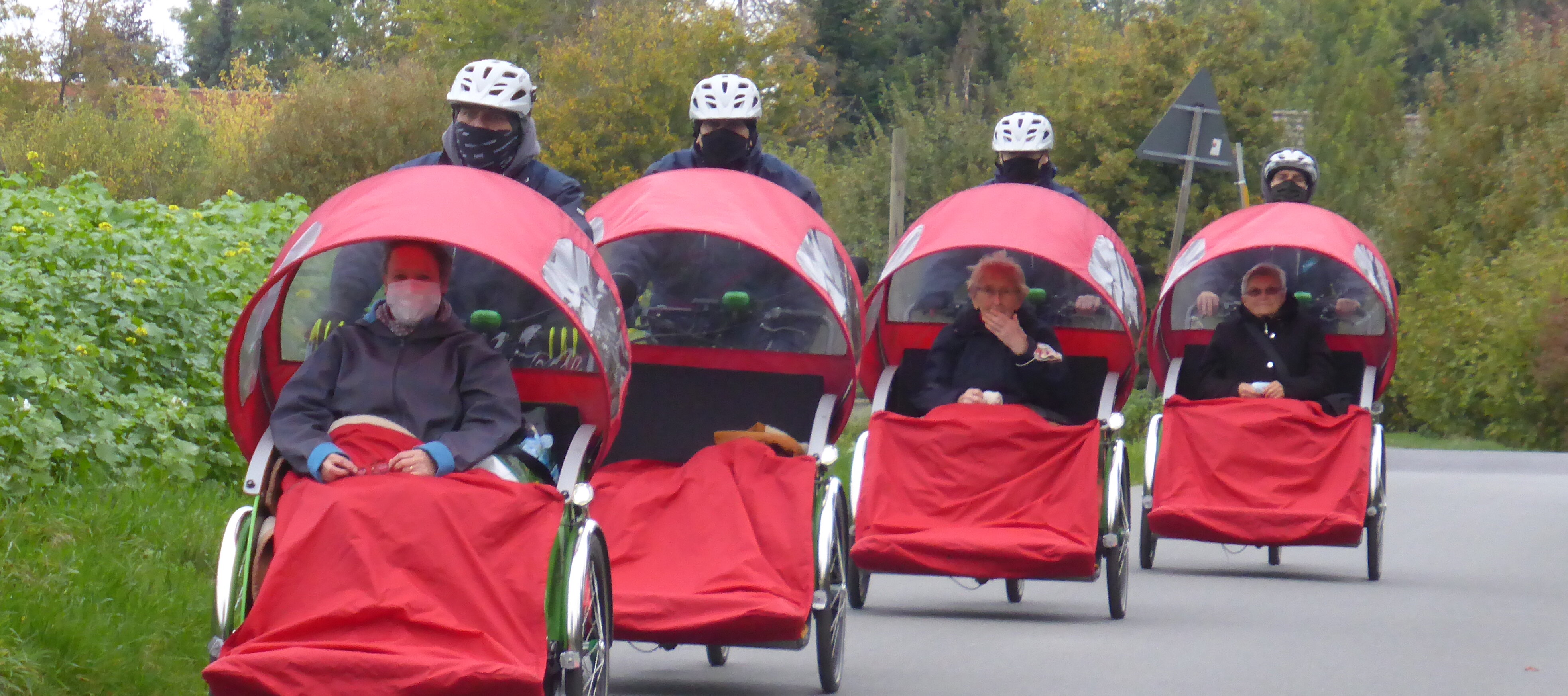 Foto: Personen, die in 4 roten Rikschas gefahren werden.