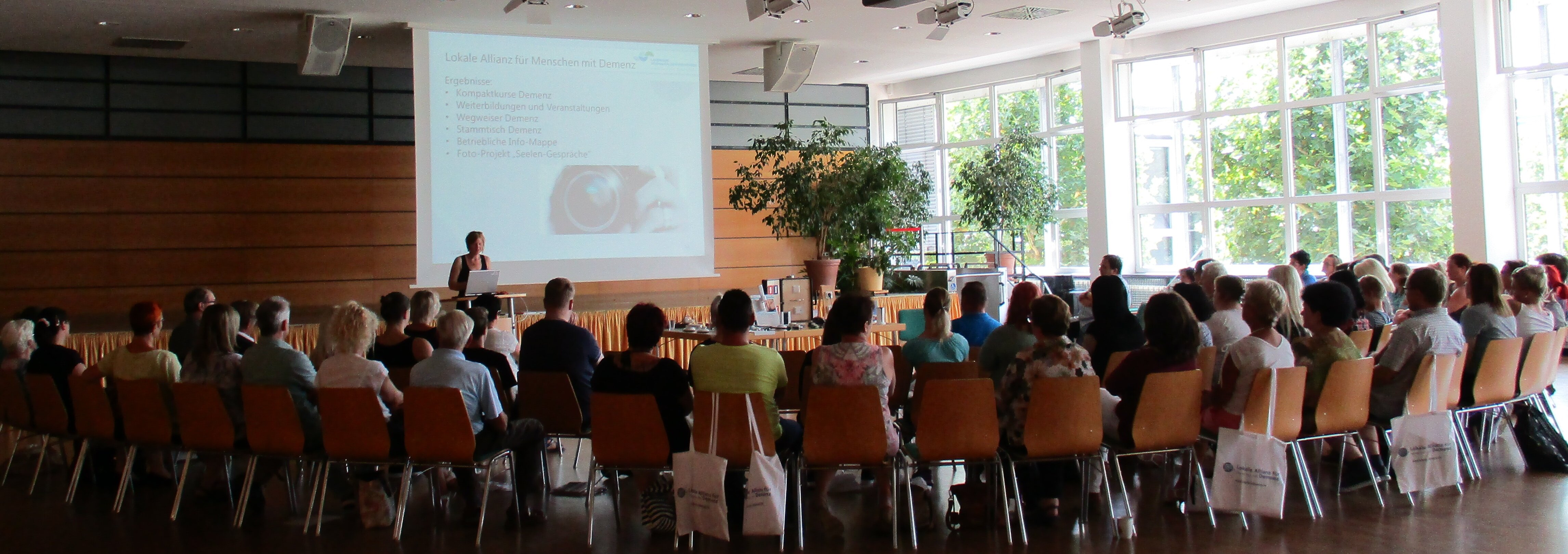 Großer Saal, in dem viele Menschen im Halbkreis sitzen. Vorne am Pult steht eine Rednerin.