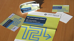 © BAGSO | Hülsmann Foto: Ausgebreitete Materialien (Plakat, Brillenputztuch, Postkarte) auf einem Tisch