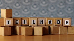 Holzklötzchen mit Buchstaben, die den Begriff "Teilhabe" bilden