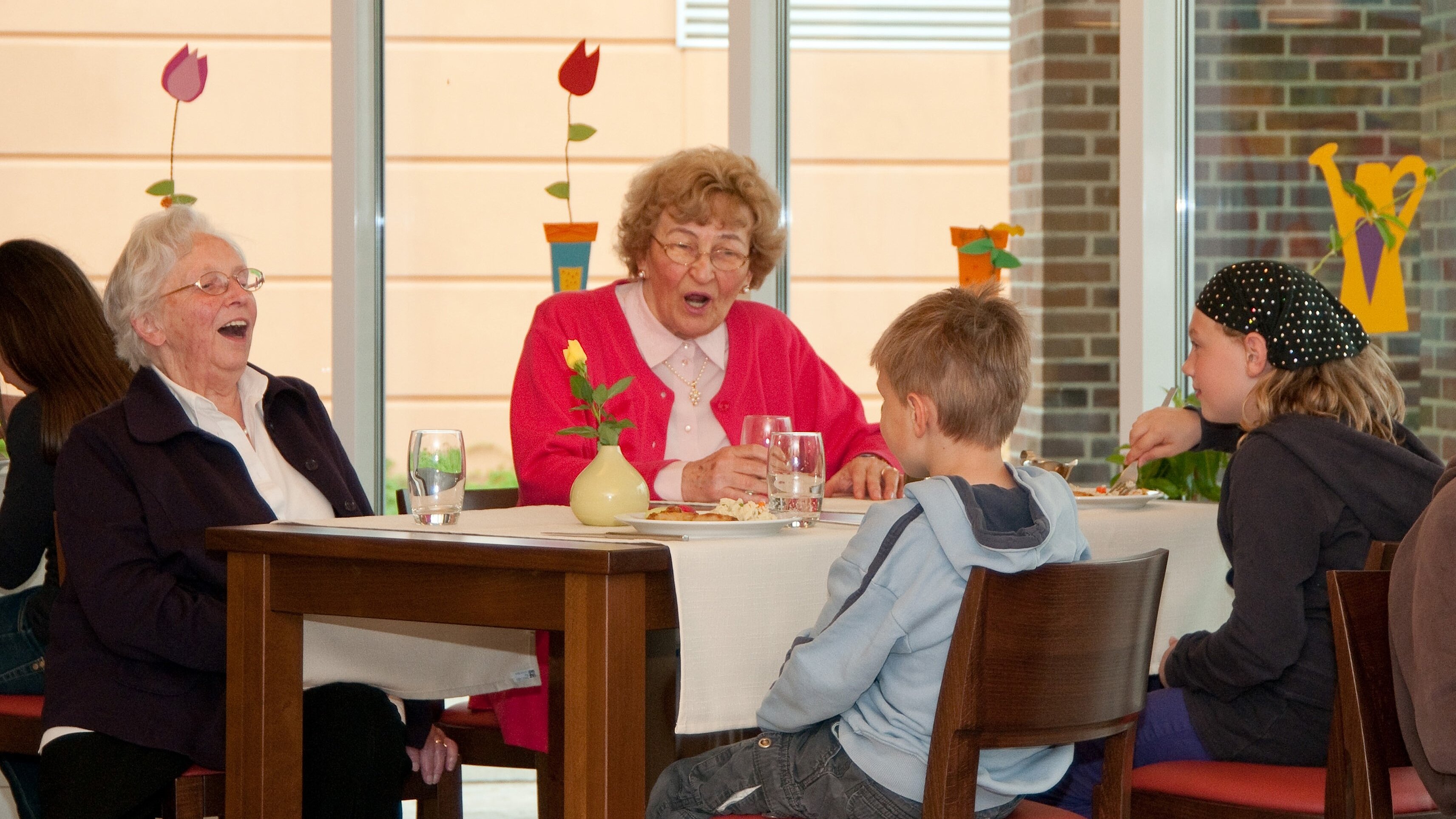 Foto: Zwei ältere Damen, die mit zwei Kindern an einem Tisch sitzen. 