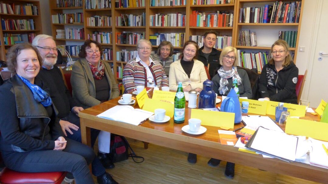 Foto: Mehrere Personen, die an einem Tisch sitzen. Im Hintergrund stehen viele Bücherregale.