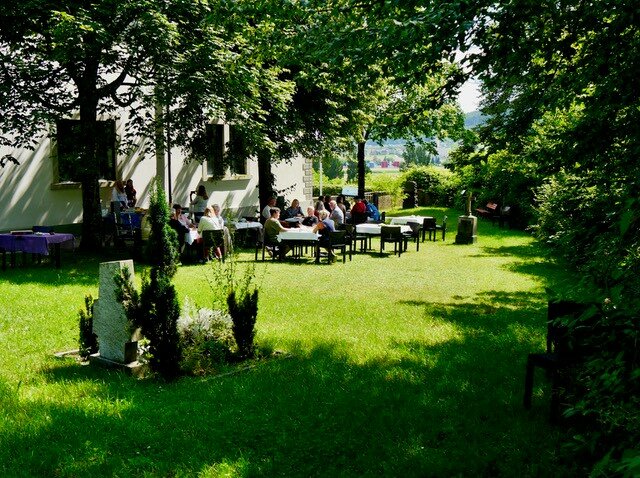 Garten neben der Kirche. Menschen sitzen an Tischen