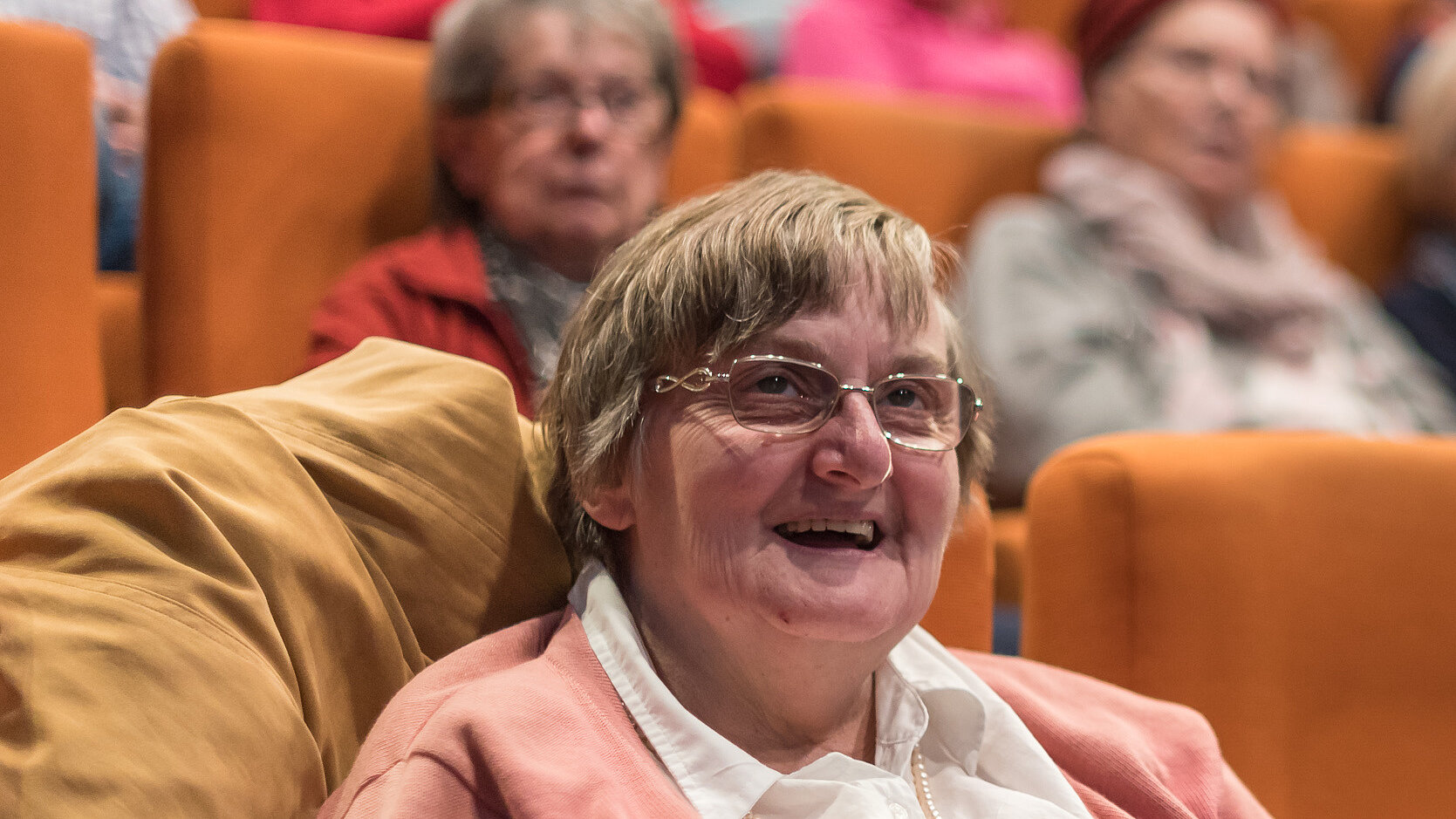 Eine ältere Dame welche in einem Kinosessel sitzt und strahlt