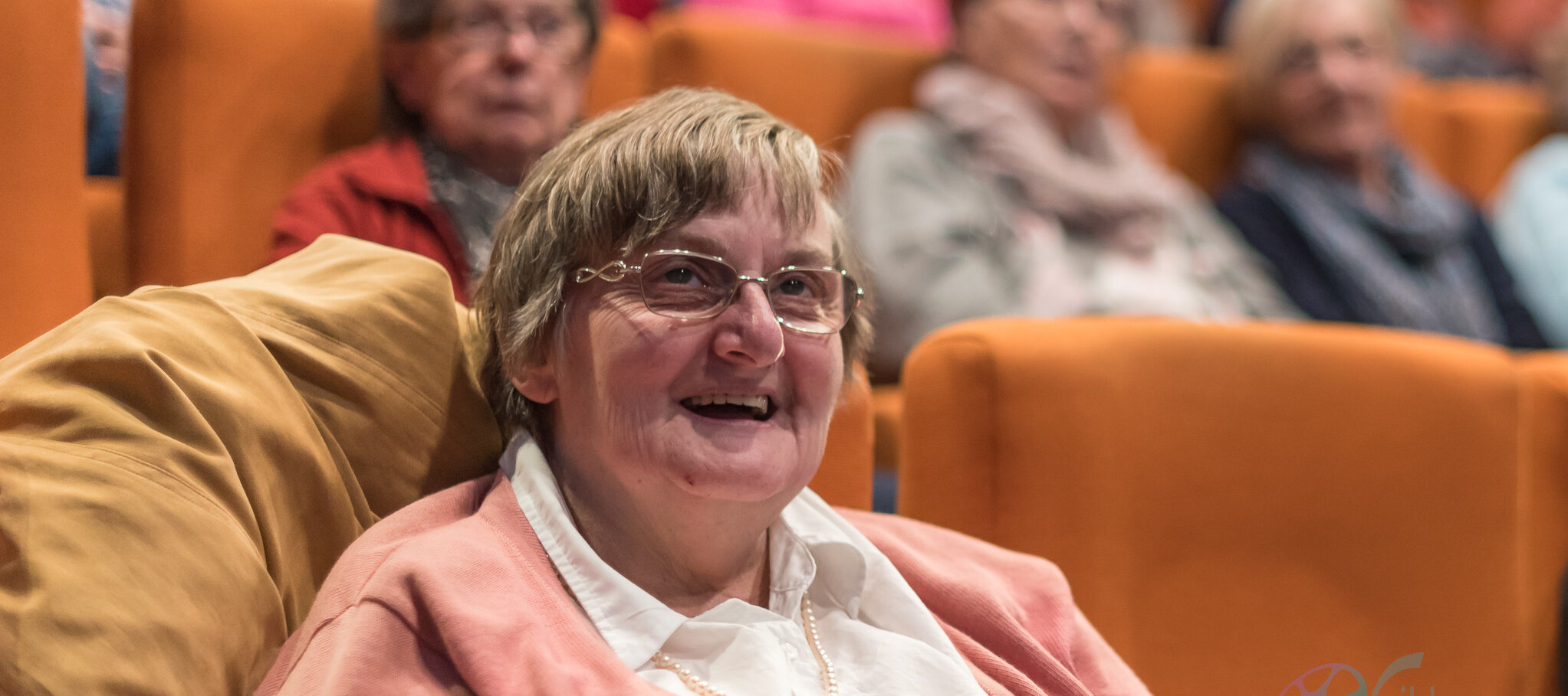 Eine ältere Dame welche in einem Kinosessel sitzt und strahlt