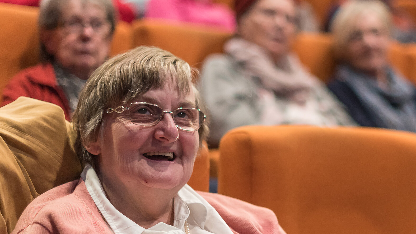 Eine ältere Dame welche in einem Kinosessel sitzt und strahlt