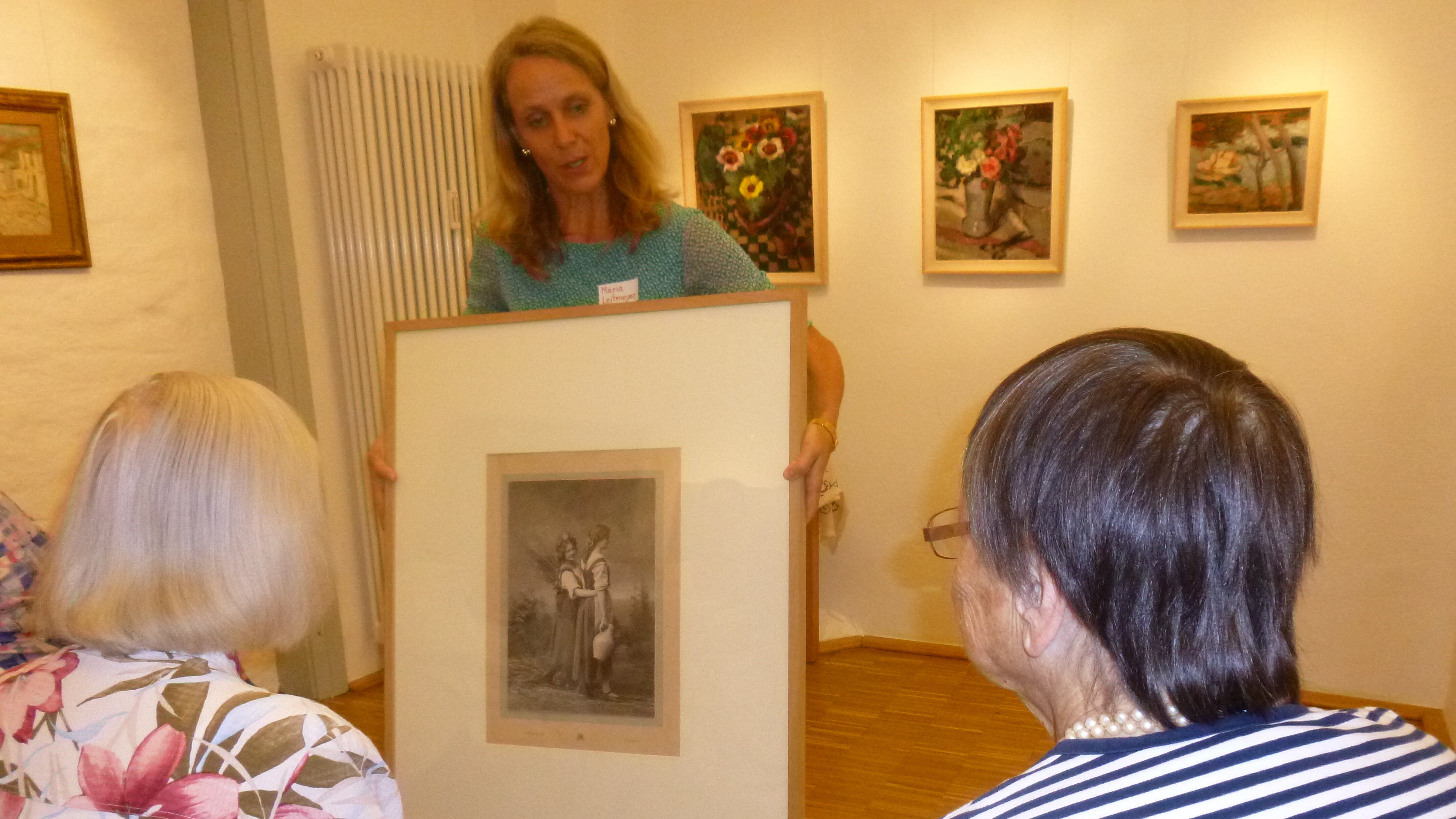 Eine Frau zeigt zwei älteren Damen ein Kunstwerk