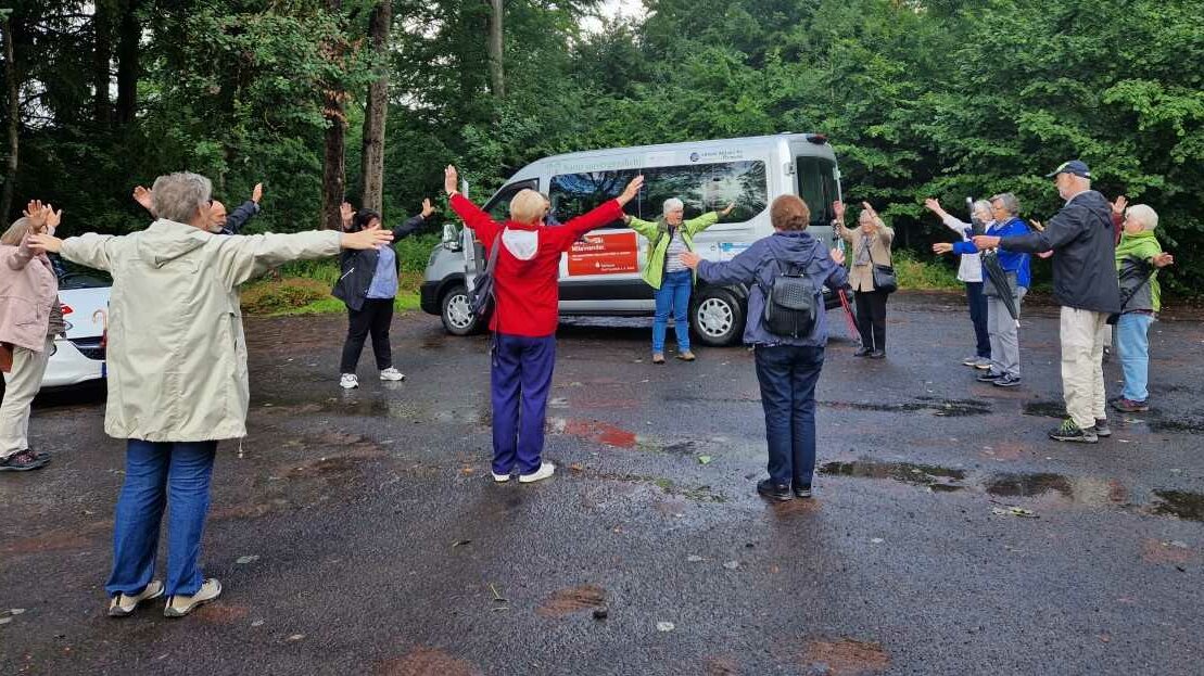 Eine Seniorengruppe macht auf einem Parkplatz Gymnastik 