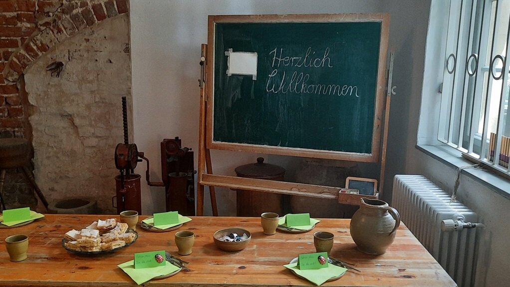 Vordergrund: Gedeckte Kaffeetafel / Hintergrund: Schultafel mit "Herzlich Willkommen"