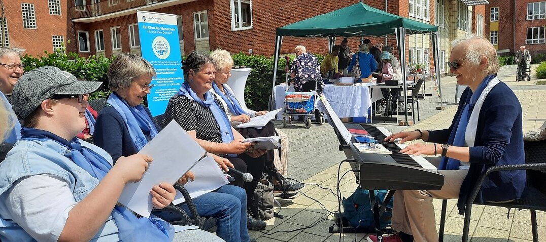 Foto: Eine Frau an einem Keyboard und singende Teilnehmer der Möllner Goldkehlen