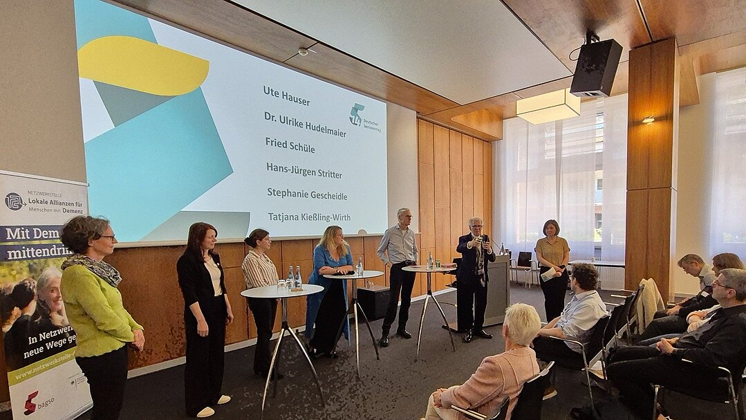 Die sechs Mitwirkenden sowie die Moderatorin stehen an Stehtischen