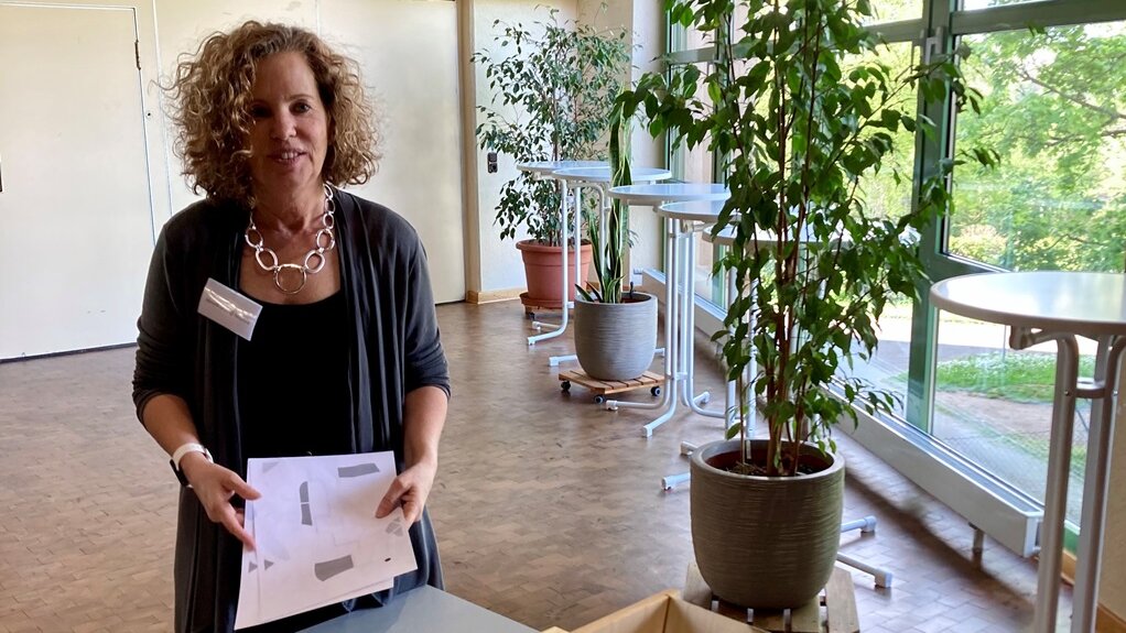 Simone Grecki-Runde steht an einem Tisch, auf dem eine Holzkiste vom Demenzparcours steht