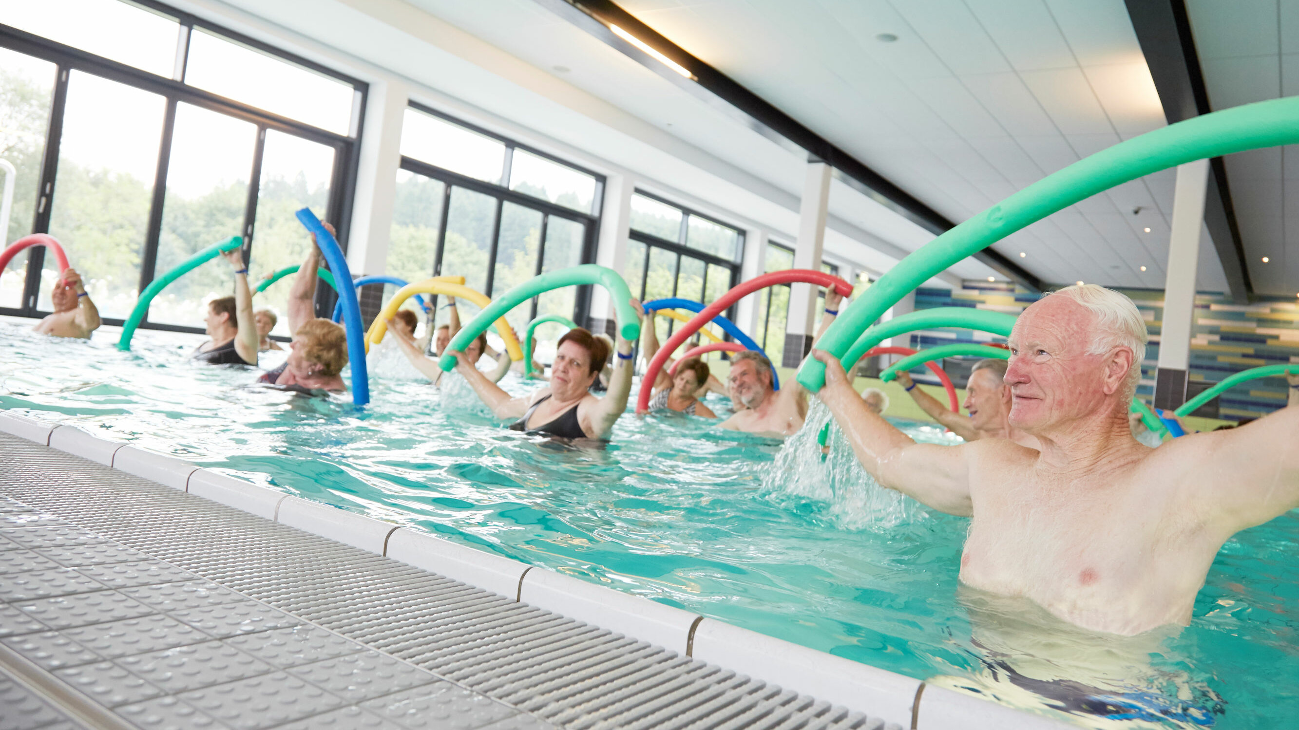 Auf dem Foto sind Senioren im Schwimmbad zu sehen. Hier werden Übungen mit einer Schwimmnudel gemacht