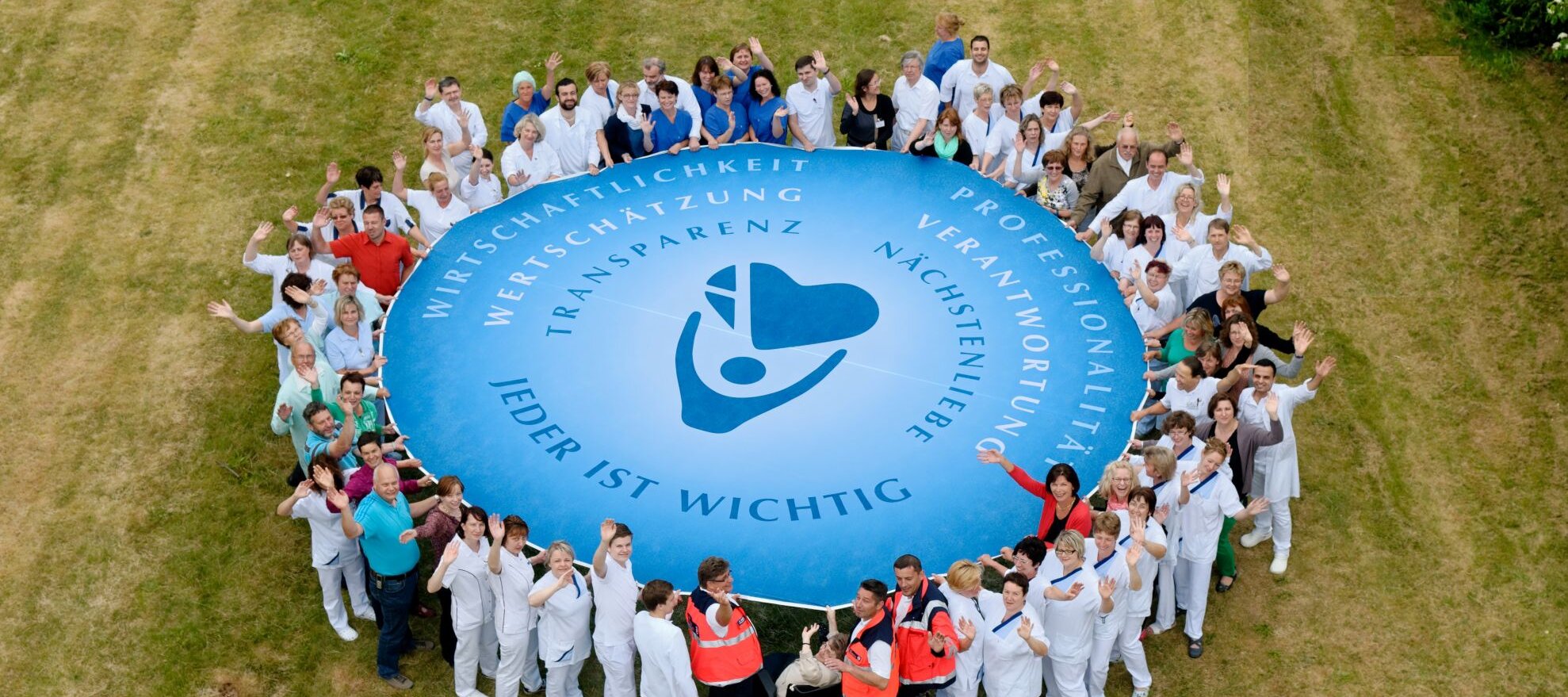 Foto: Vogelperspektive: Das Personal des Krankenhauses hält ein Schwungtuch mit Logo der Agaplesion gAG