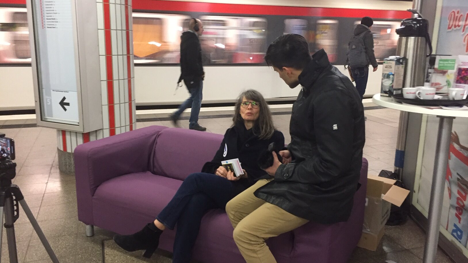 Foto: Lila Sofa mit 2 Personen drauf steht auf einem U-Bahnsteig