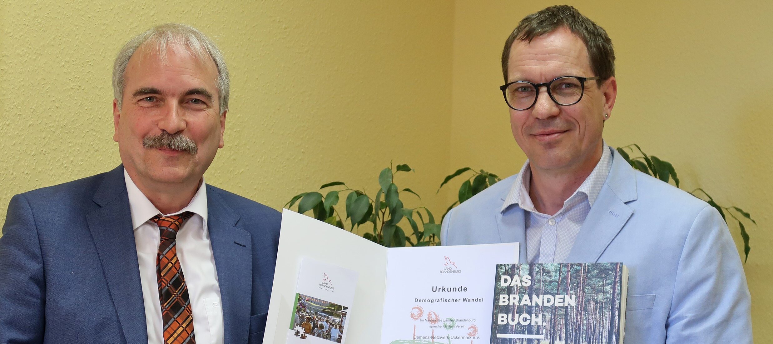 Foto: Zwei Herren werden fotografiert. Ein Mann hält eine Auszeichnung hoch.