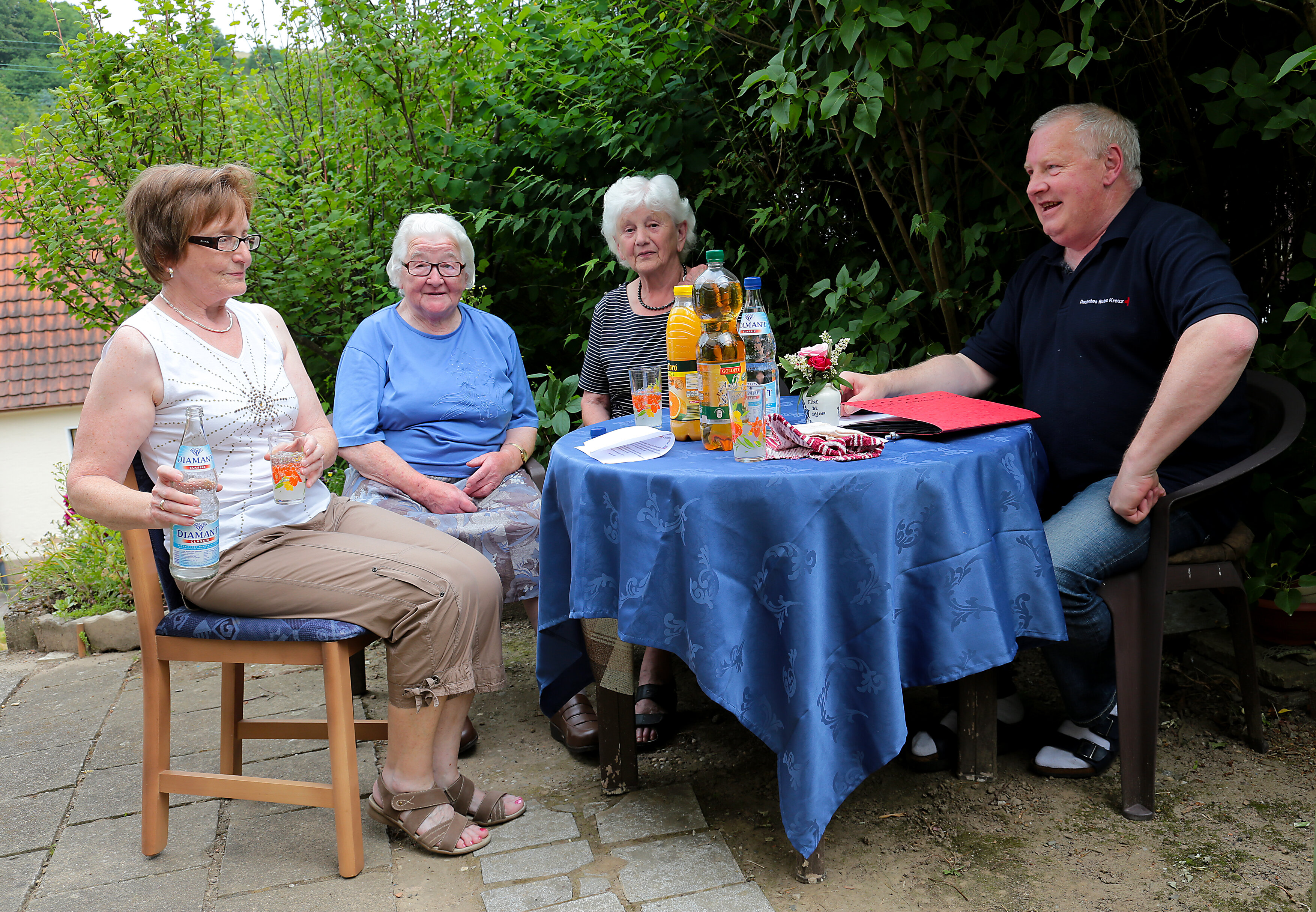 Die Dorfschwester Annetraud Kling sitzt mit zwei älteren Damen und einem Herrn vom Deutschen Roten Kreuz an einem Gartentisch 