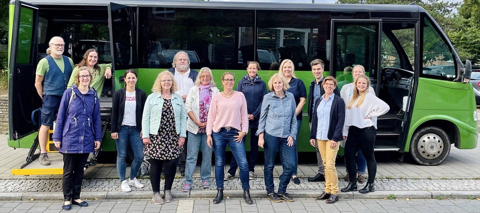 Foto: Gruppenfoto mit 15 Männern und Frauen aus der Lokalen Allianz vor dem grünen Bus