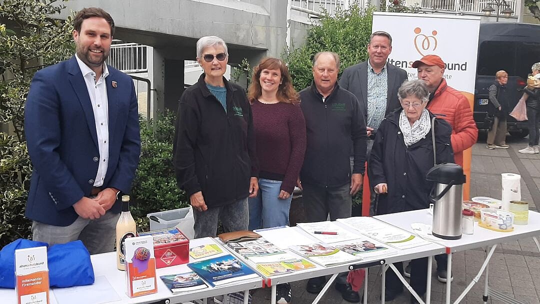 Foto: Mehrere Personen stehen im Freien hinter einem langen weißen Klapptisch, auf dem Infomaterial liegt.
