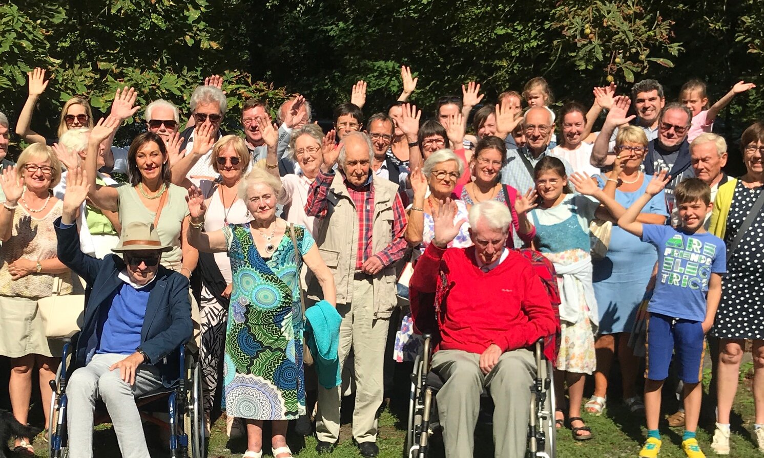 Gruppenbild von Menschen unterschiedlichen Alters, die in die Kamera winken