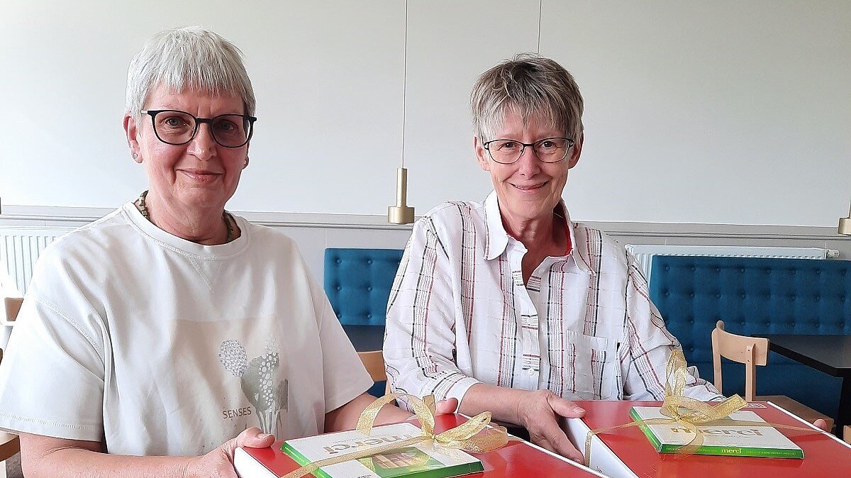 Foto: Zwei lächelnde Seniorinnen halten ein Geschenk mit Pralinen in der Hand.