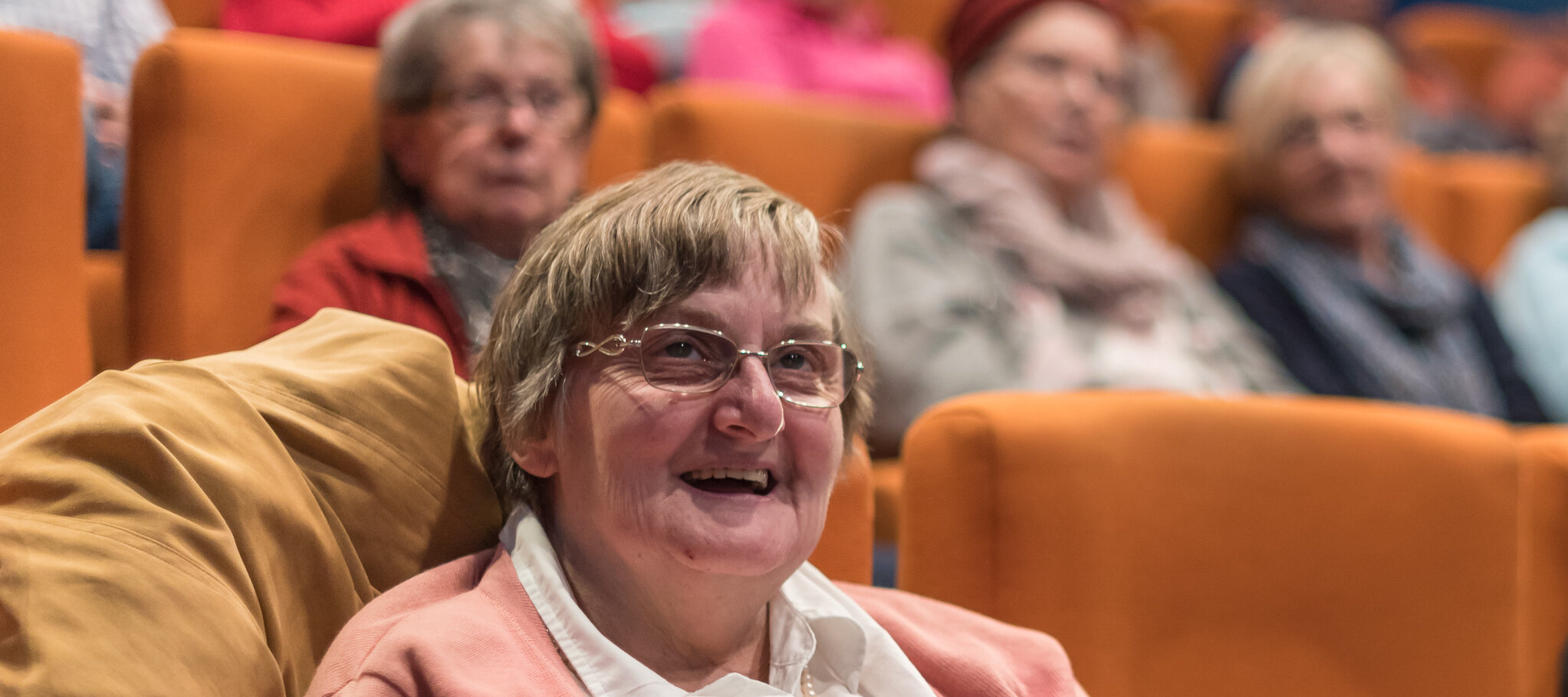 Eine ältere Dame welche in einem Kinosessel sitzt und strahlt