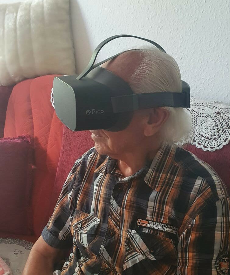 Ein älterer Mann sitzt auf dem Sofa. Er trägt eine Virtual-Reality-Brille 