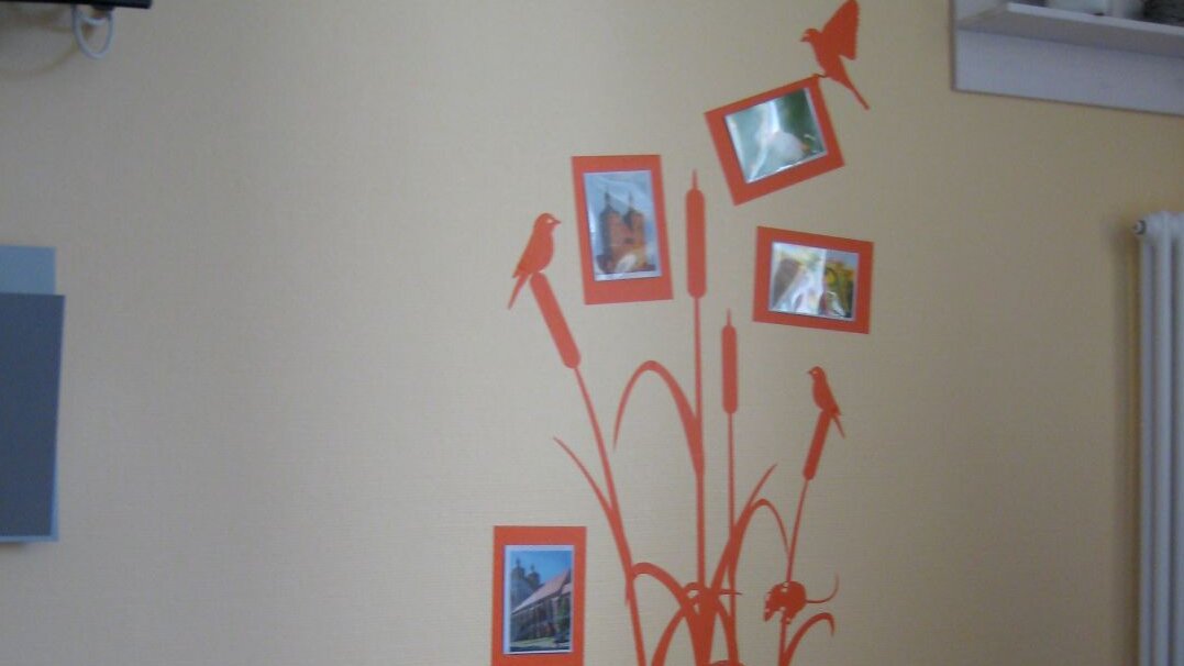 Foto: Blick in ein Patientenzimmer, dessen Wand durch eine Wandillustration und Fotos optisch gestaltet ist