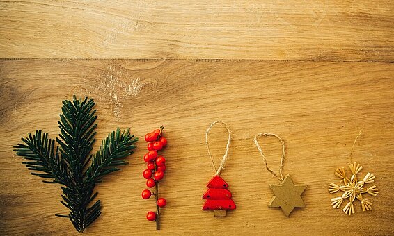 Blick von oben auf einen Holztisch: Nebeneinander liegen ein Tannenzweig und mehrere Holzanhänger für den Weihnachtsbaum