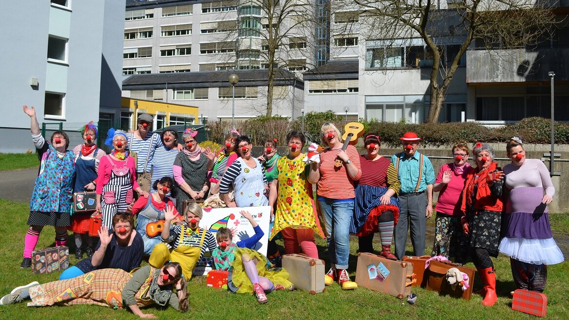 Gruppenbild von Frauen und Männern auf einer Wiese. Alle sind als Clowns verkleidet. 