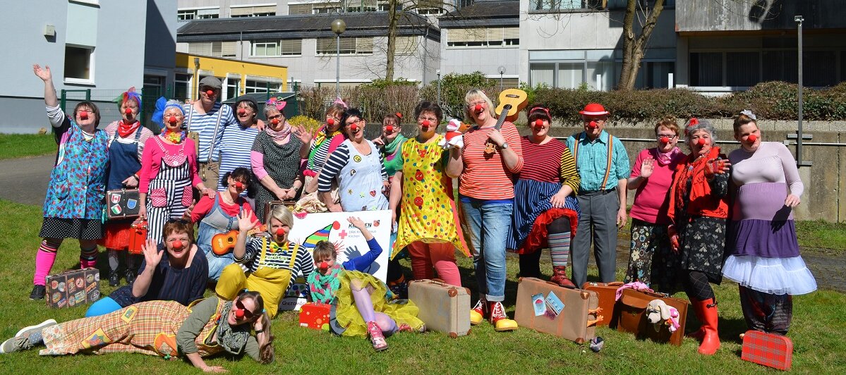Gruppenbild von Frauen und Männern auf einer Wiese. Alle sind als Clowns verkleidet. 