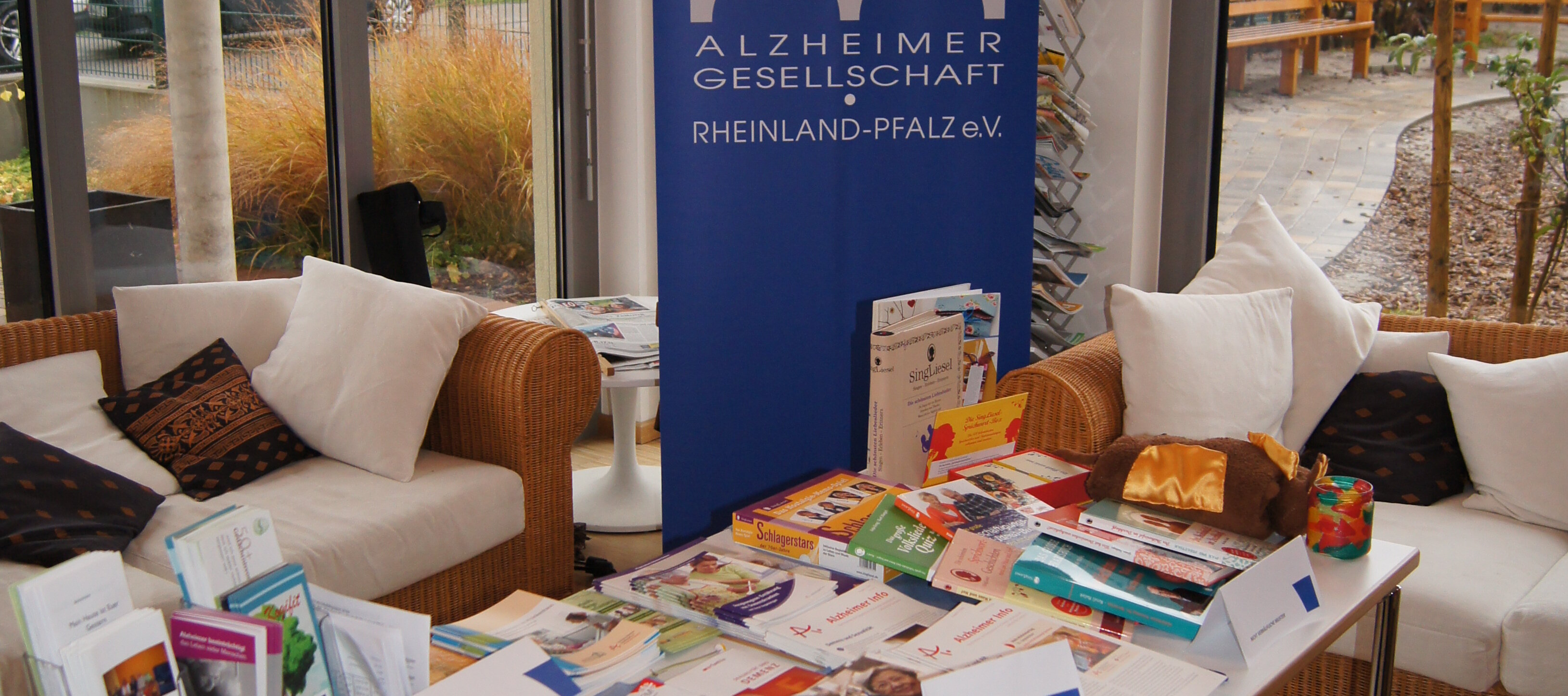 Ein Tisch, auf dem viele Informationsmaterialien der Alzheimergesellschaft liegen. Im Hintergrund steht ein Roll Up der Alzheimergesellschaft.