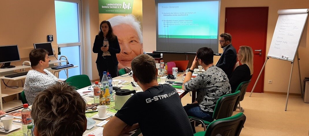 Foto: Personengruppe bei einer Präsentation mit Vortrag.