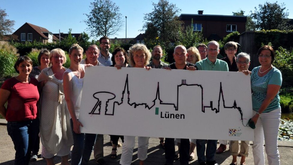 Aktive des Netzwerkes Demenz – Netzwerkseminar 2018 Auf diesem Foto sehen Sie viele Personen, die ein Schild mit der Stadtsilhouette von Lünen hochhalten