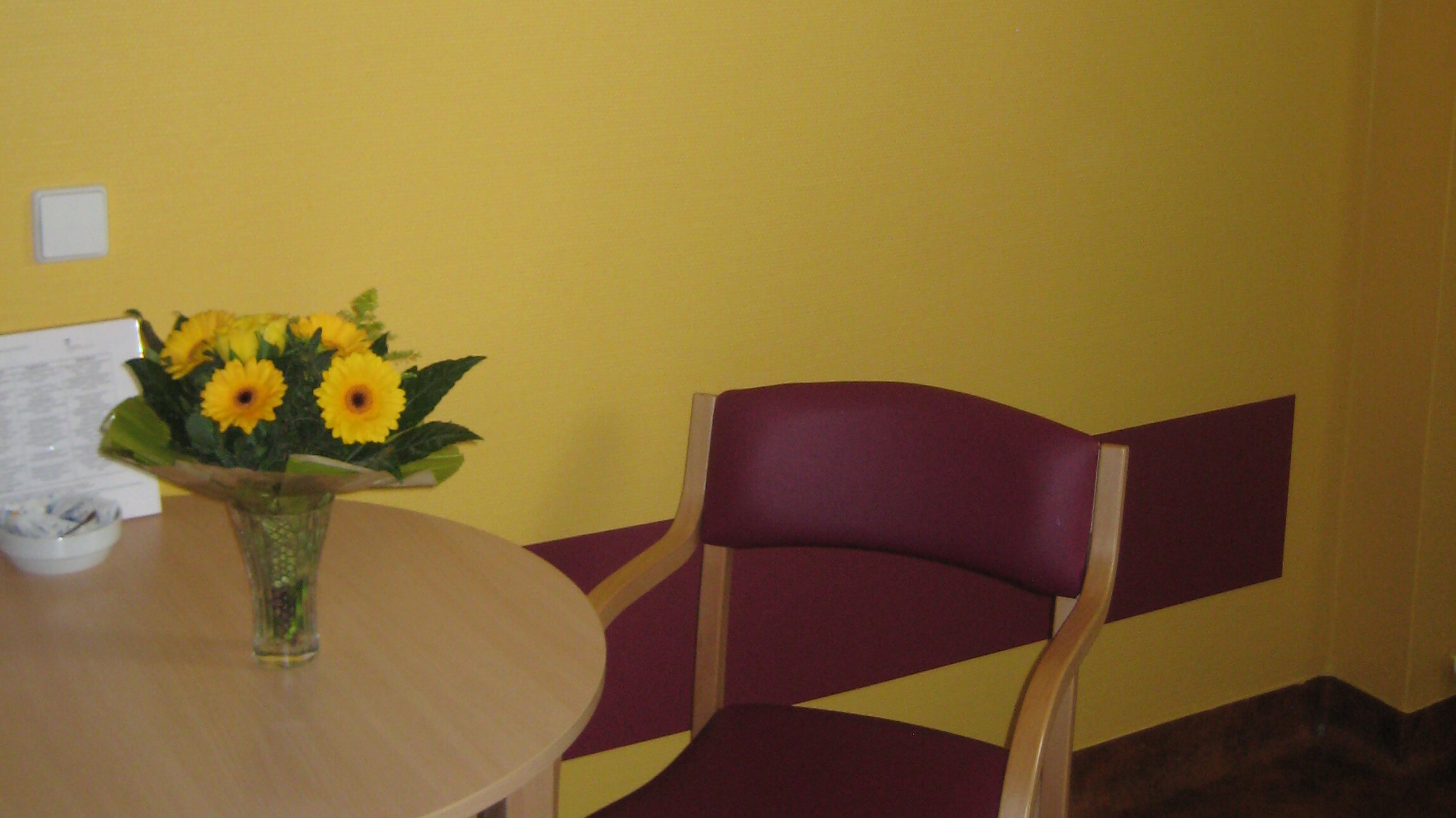 Blick in ein gelb gestrichenes Patientenzimmer, das auch durch Bilder an der Wand Orientierung gibt 