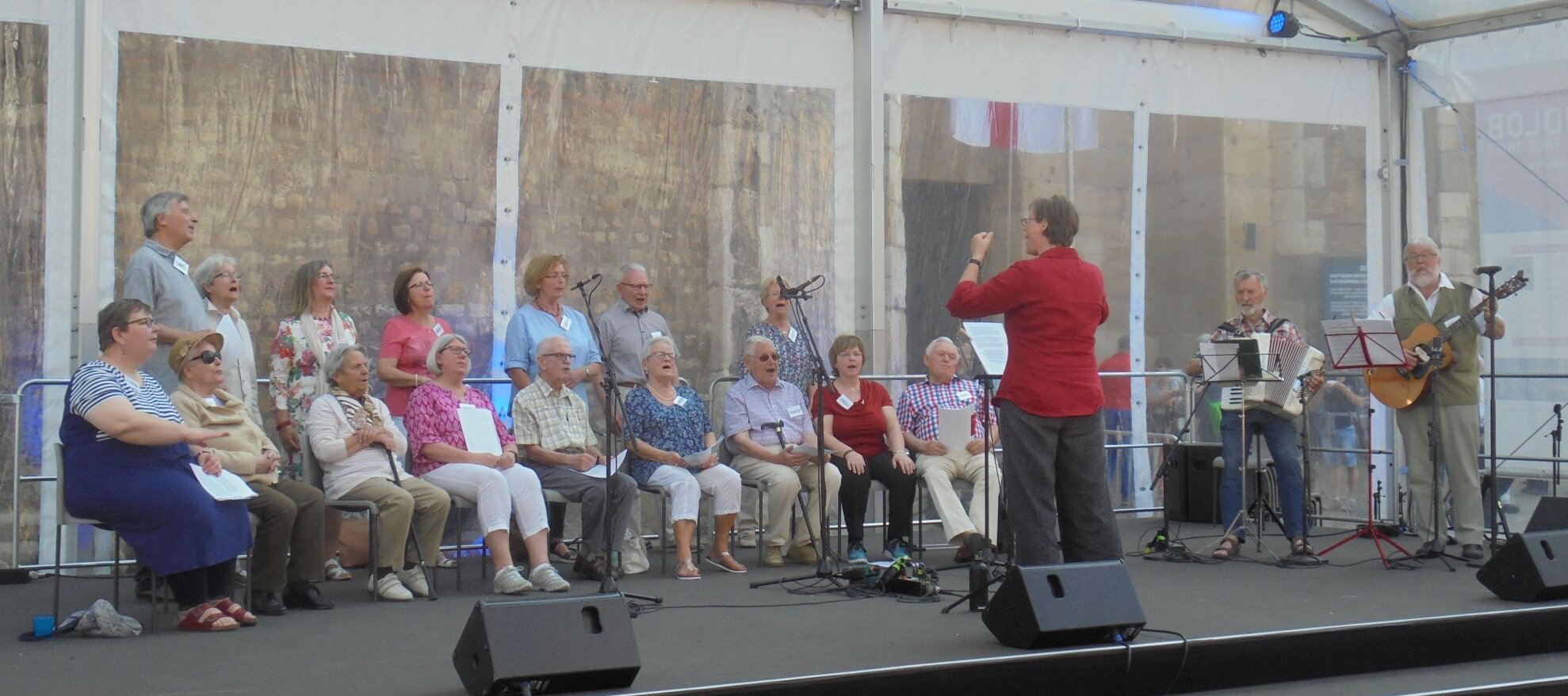 Foto: Foto von einem Chorauftritt mit Dirigentin, einem Akkordeonspieler und einem Gitarristen