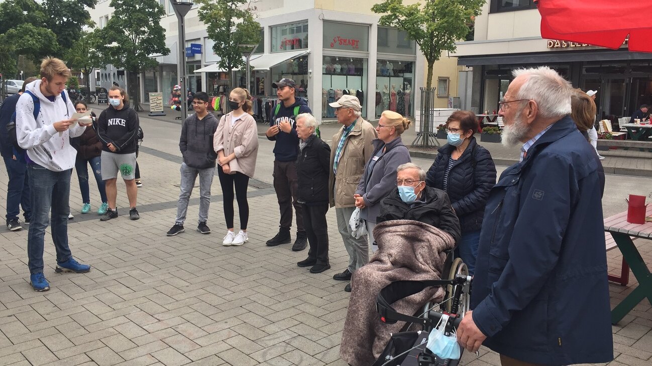 Foto: Ältere Menschen, Schülerinnen und Schüler hören Schülervortrag