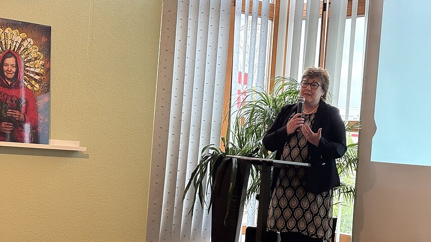 Auftaktveranstaltung am 25. April 2025: Petra Grimm-Benne, Ministerin für Arbeit, Soziales, Gesundheit und Gleichstellung begrüßt die Anwesenden. Foto: Petra Grimm-Benne hält Rede an Rednerpult auf einer Bühne eines Veranstaltungsraums vor einer Leinwand stehend.