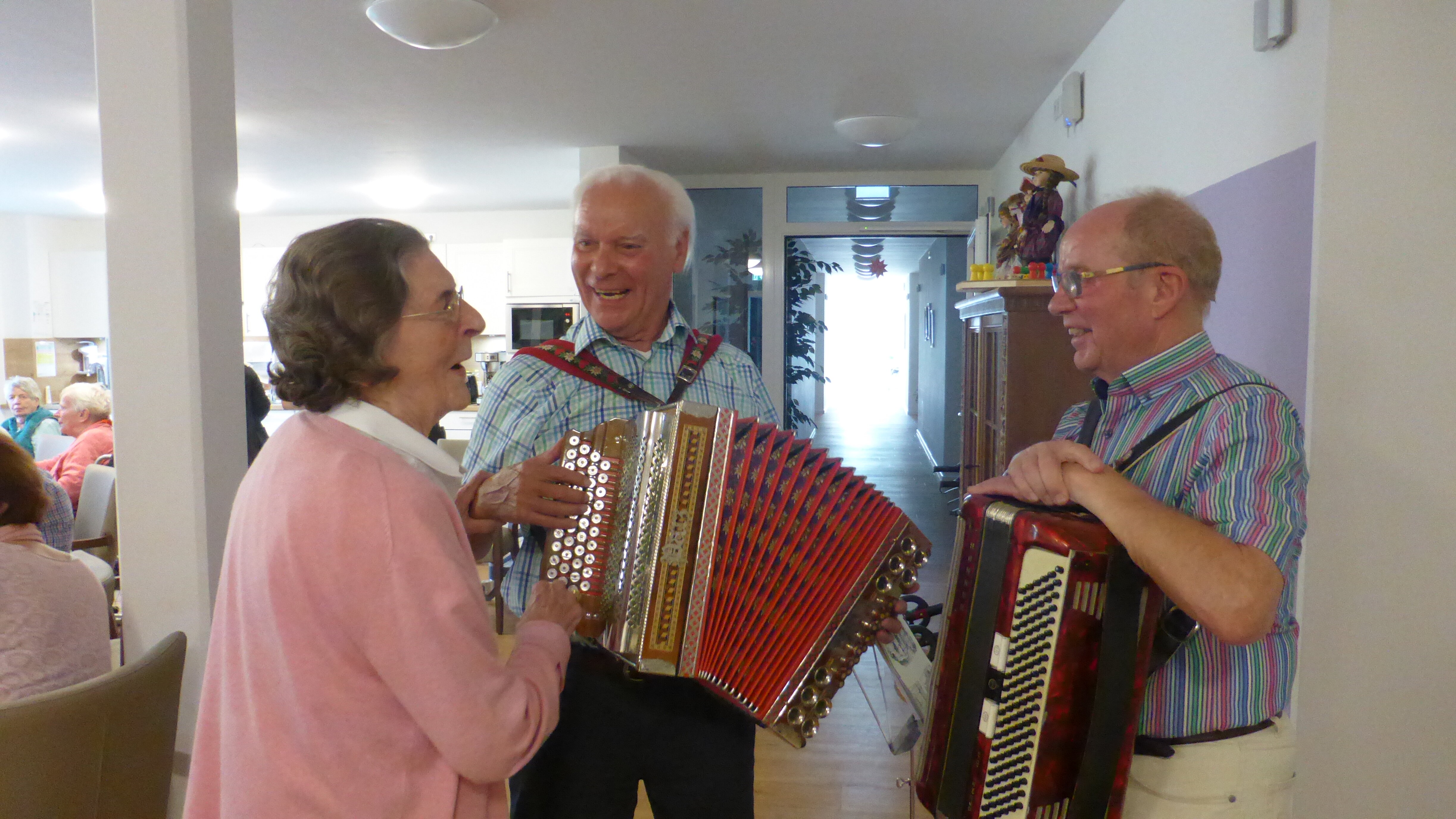 Zwei lächelnde Männer mit jeweils einer Ziehharmonika und eine ältere Dame.