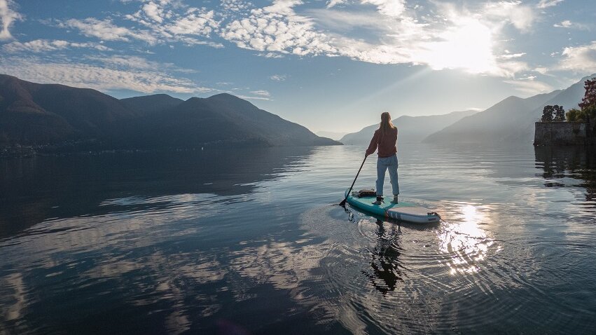 Person beim Standup-Paddling auf einem See im Abendlicht 