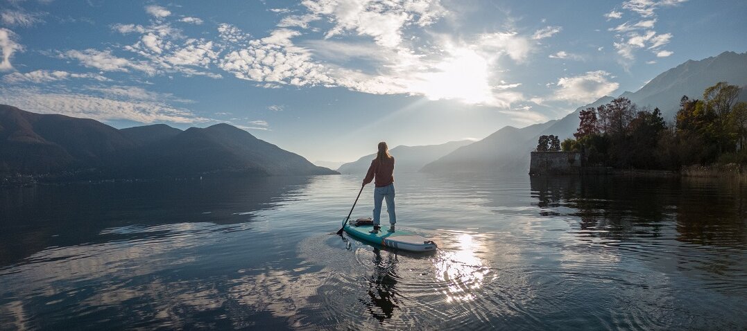 Person beim Standup-Paddling auf einem See im Abendlicht 