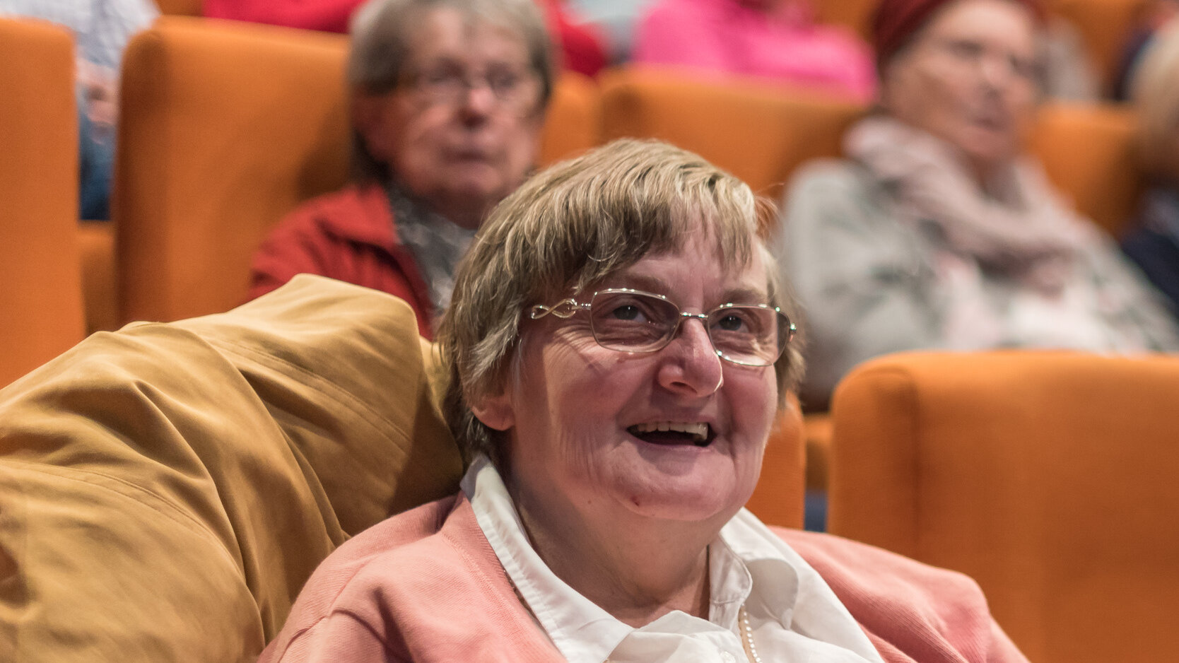 Mehrere ältere Menschen sitzen in einem Kinosaal. Im vorderen Teil des Fotos sieht man eine lachende Zuschauerin.
