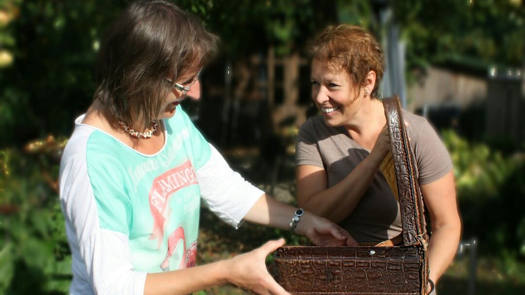 Foto: Zwei Frauen, die sich draußen den Inhalt eines kleinen Koffers ansehen.