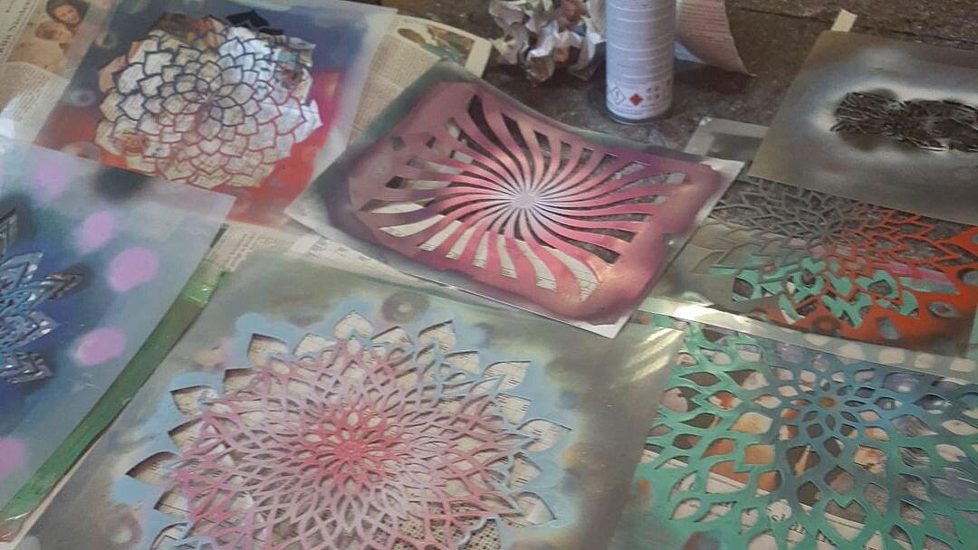 Foto: 7 farbig angesprühte Scherenschnitte von Mandalas liegen auf einem Tisch.