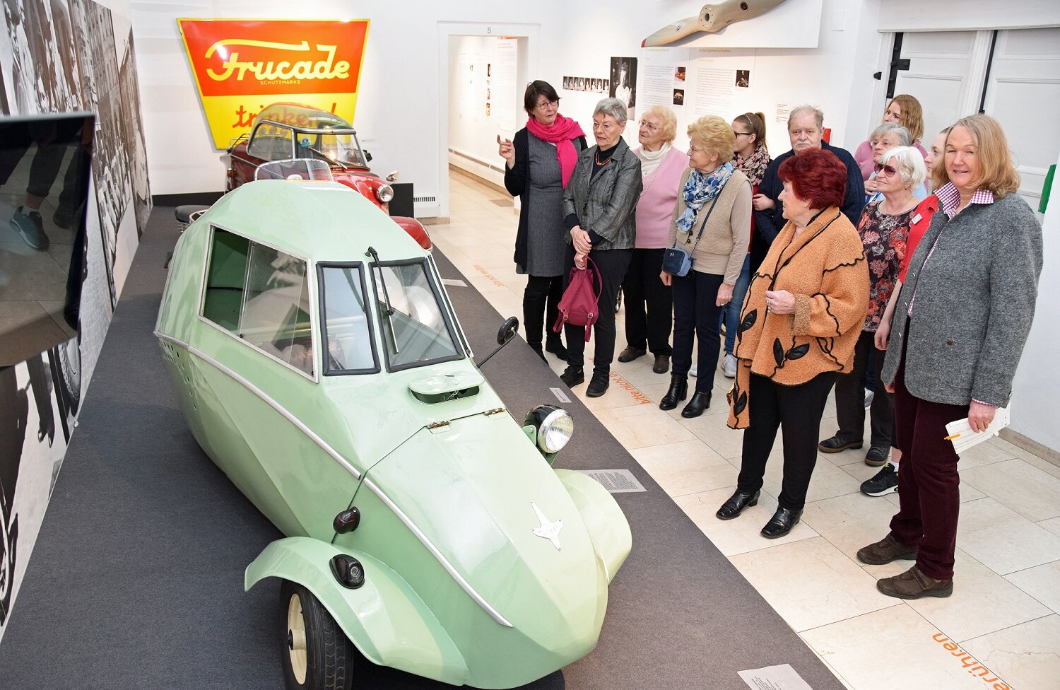 Eine Gruppe von Seniorinnen und Senioren betrachtet in der Städtischen Galerie Rosenheim einen lindgrünen Oldtimer