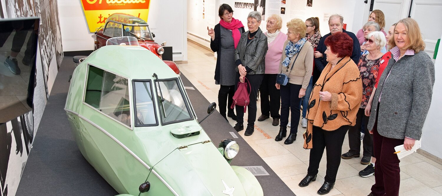 Eine Gruppe von Seniorinnen und Senioren betrachtet in der Städtischen Galerie Rosenheim einen lindgrünen Oldtimer